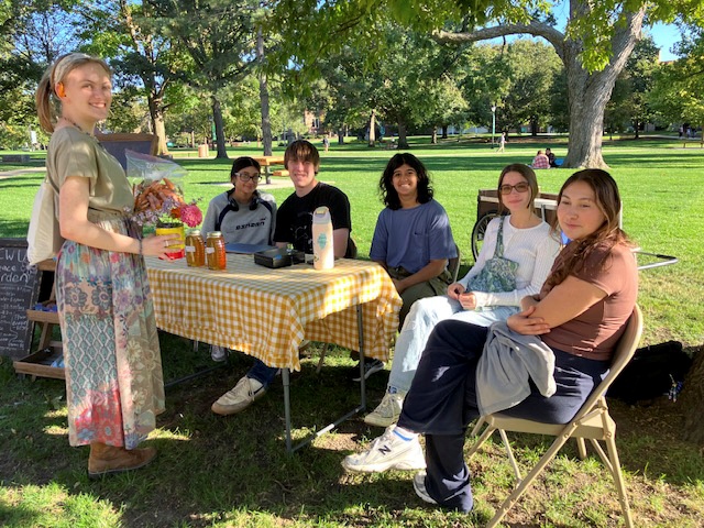 A group of students sitting at an outdoor table in the shade of a tree