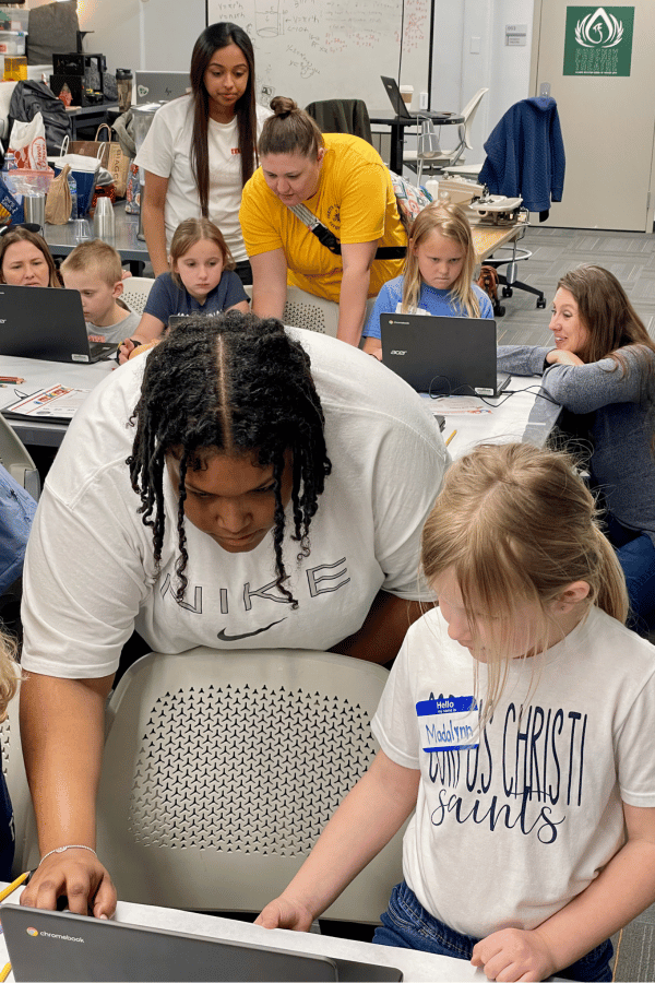 Makergirl IWU students lean over tables to help children with 3d printing software on laptops