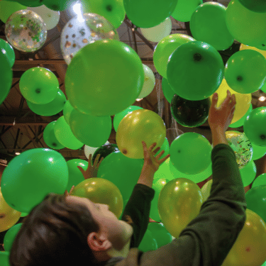 Student lifting hands to green balloons falling from the ceiling