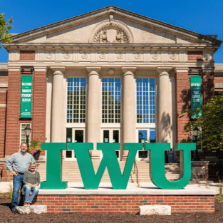 Corey and Pam Schieler posed with large steel green IWU letters outside Hansen Student Center