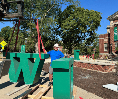 Corey Schieler stands next to the W from the IWU letters as they were being installed