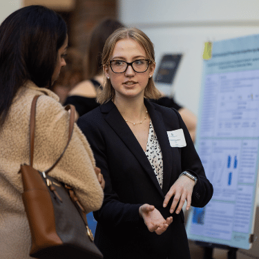 Illinois Wesleyan student presents from poster board at 2024 John Wesley Powell Student Research Conference