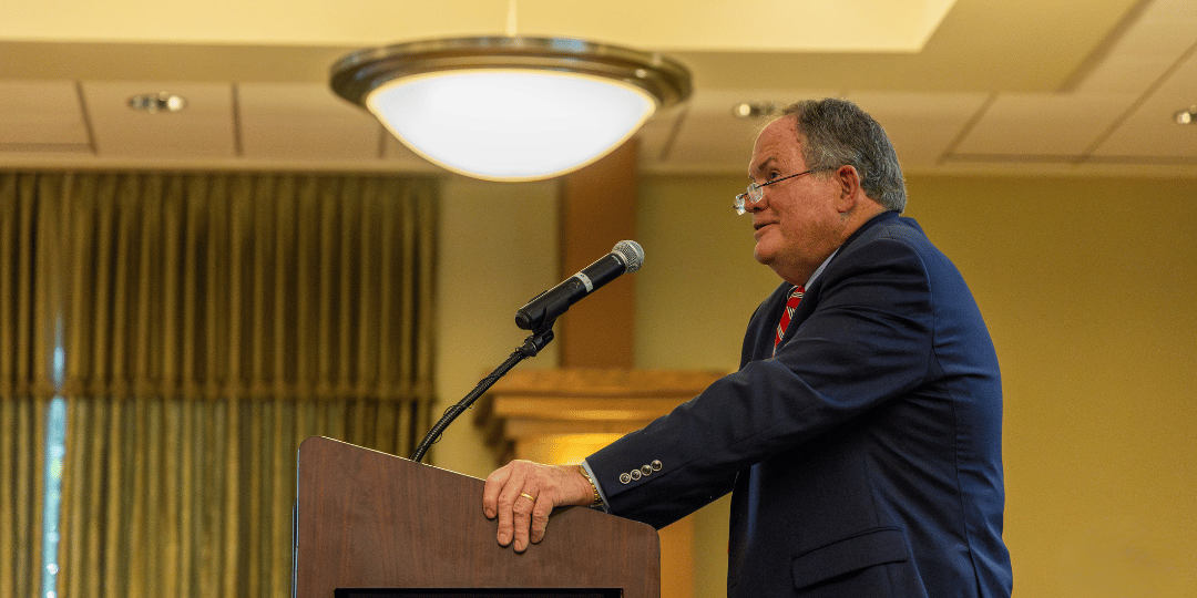 Ed Rust Jr speaks at a podium at Illinois Wesleyan University