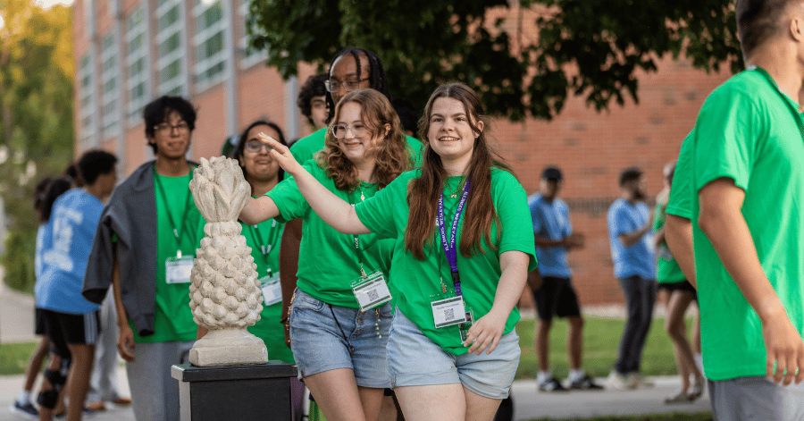 Illinois Wesleyan students file past a concrete pineapple on a pedestal and each give it a tap outside IWU's Shirk Center
