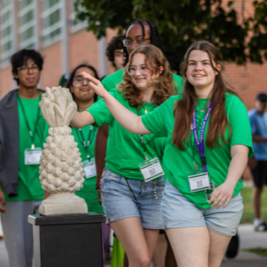 new students in green shirts tap a concrete pineapple