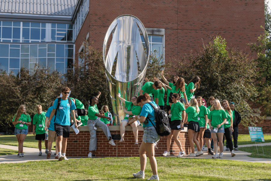students wave while sitting on the edge of a fountain on IWU's campus
